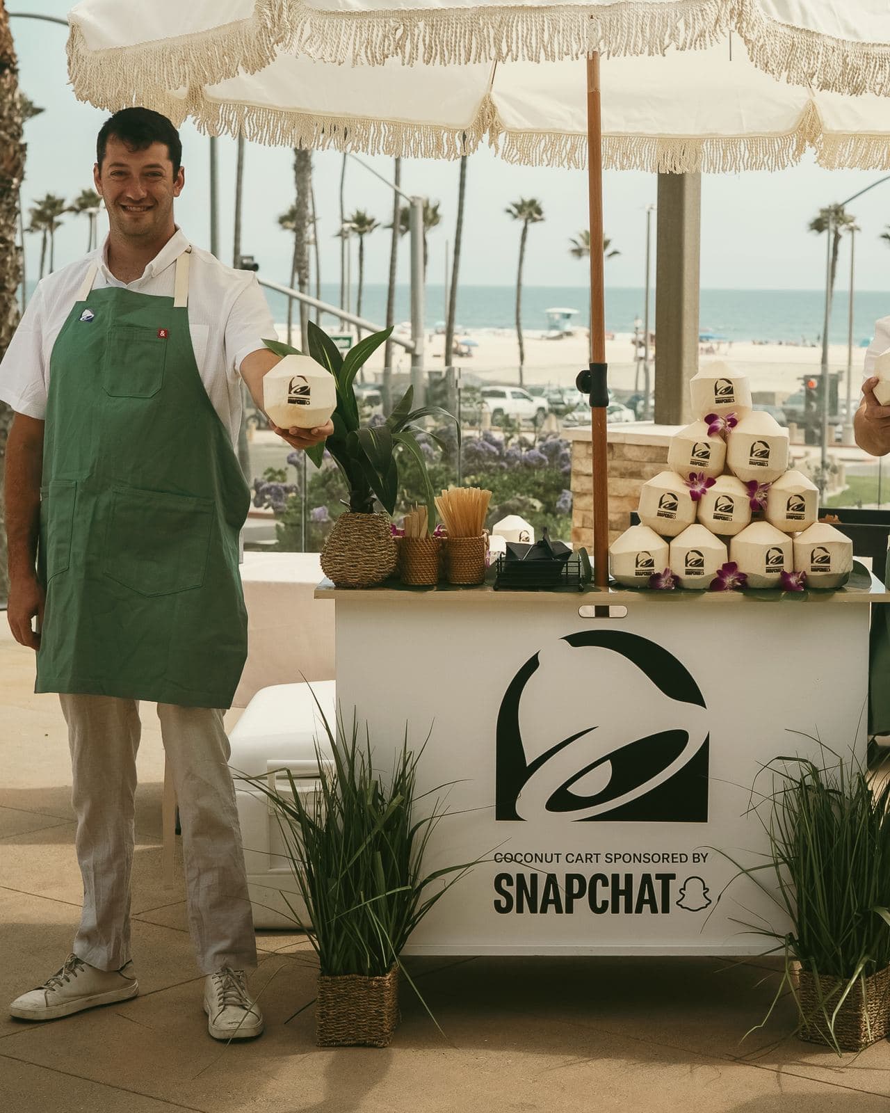Taco Bell coconut cart sponsored by Snapchat, two specialists in green aprons, beach behind