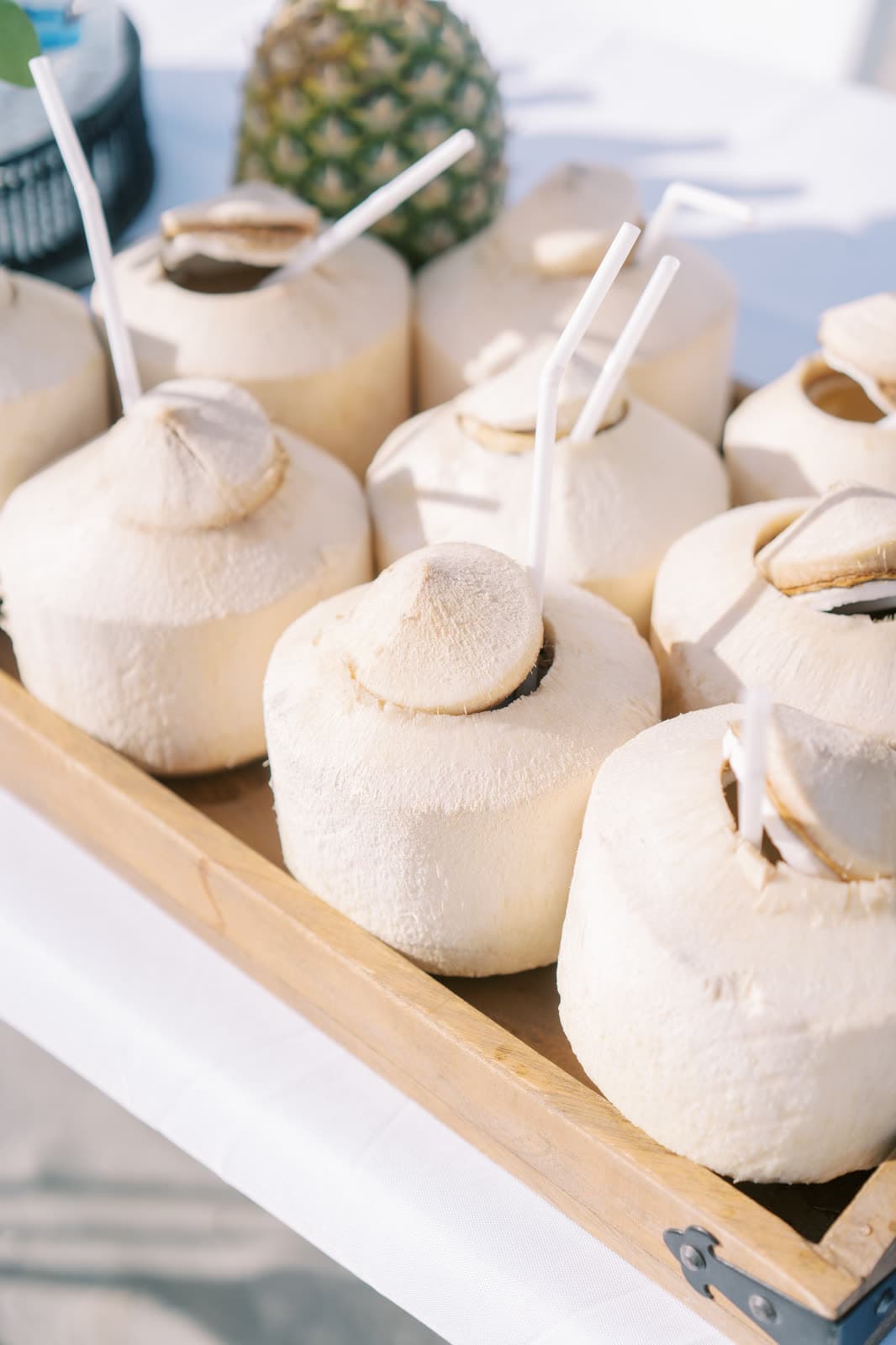 Tray of opened coconuts with straws at a beach wedding