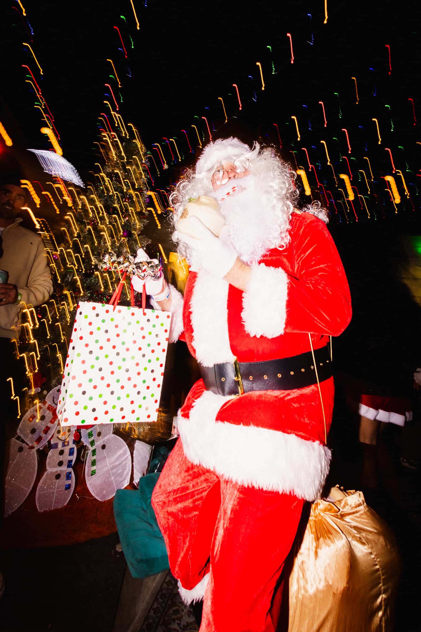 Santa in a full red suit and white beard drinking from a coconut through a striped straw