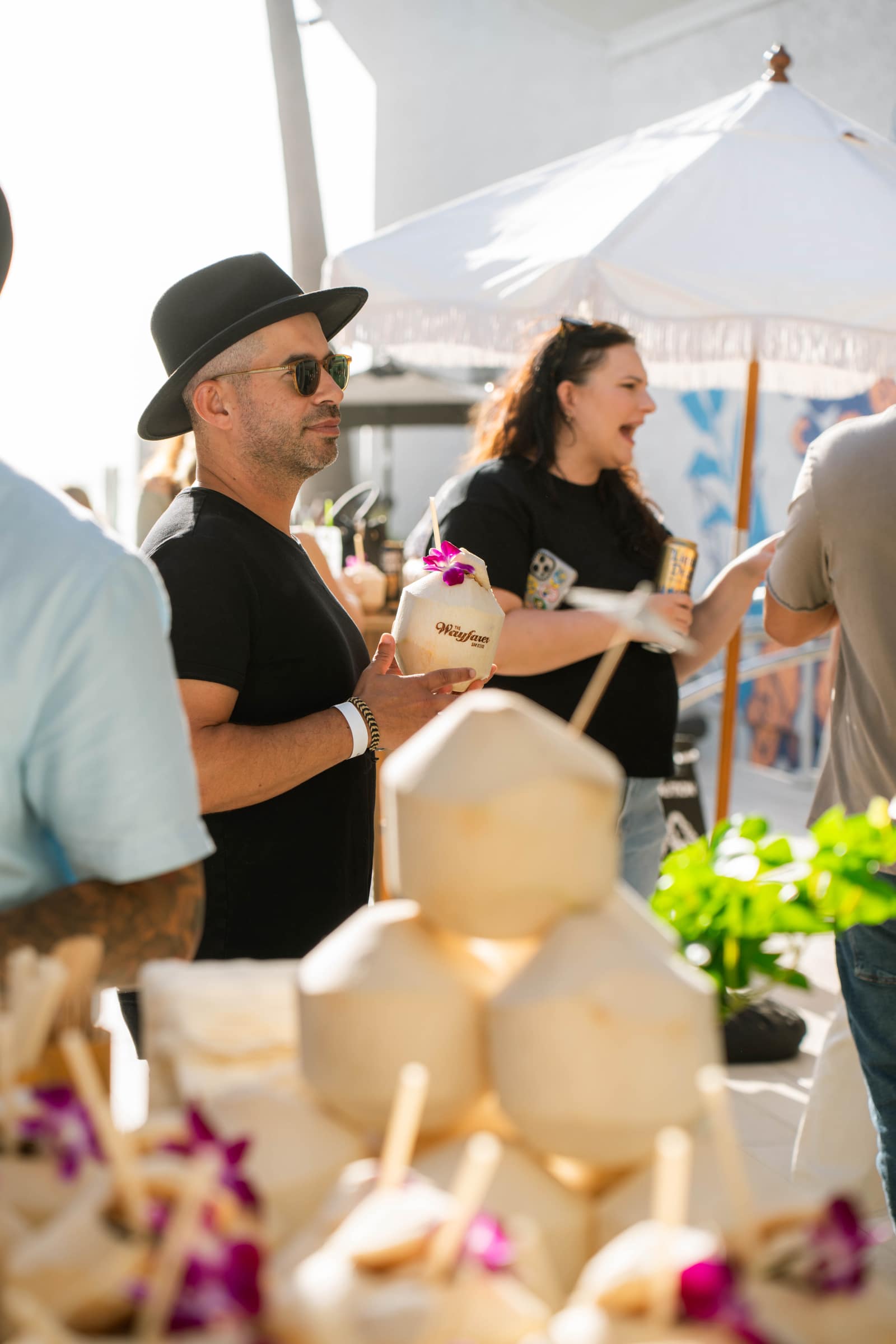 a stacked pyramid of opened custom coconuts with straws and orchids, guests reaching in behind it
