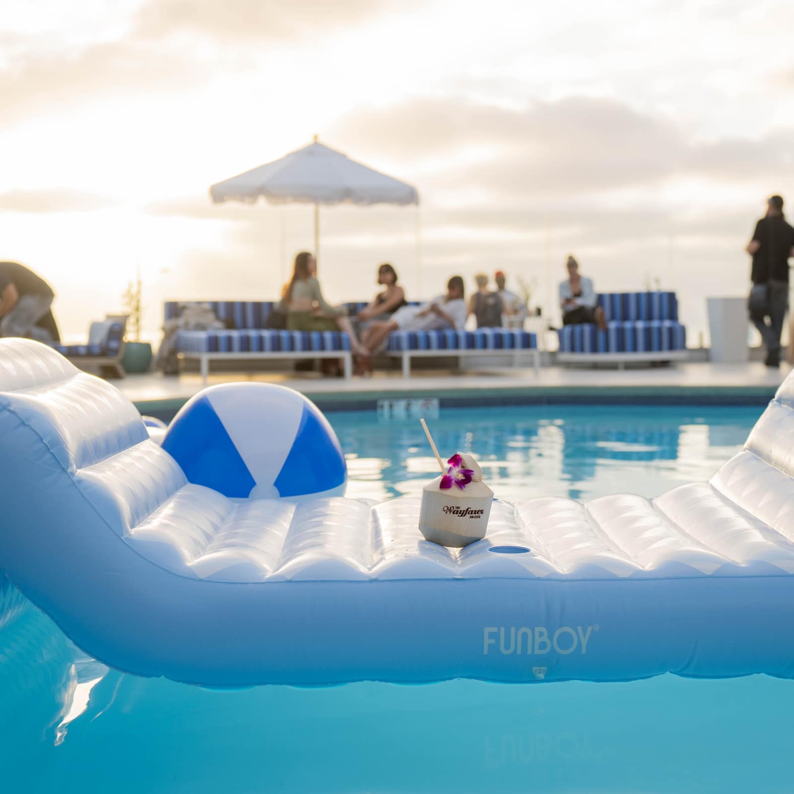 a single custom coconut with an orchid floating on an inflatable pool lounger next to a beach ball